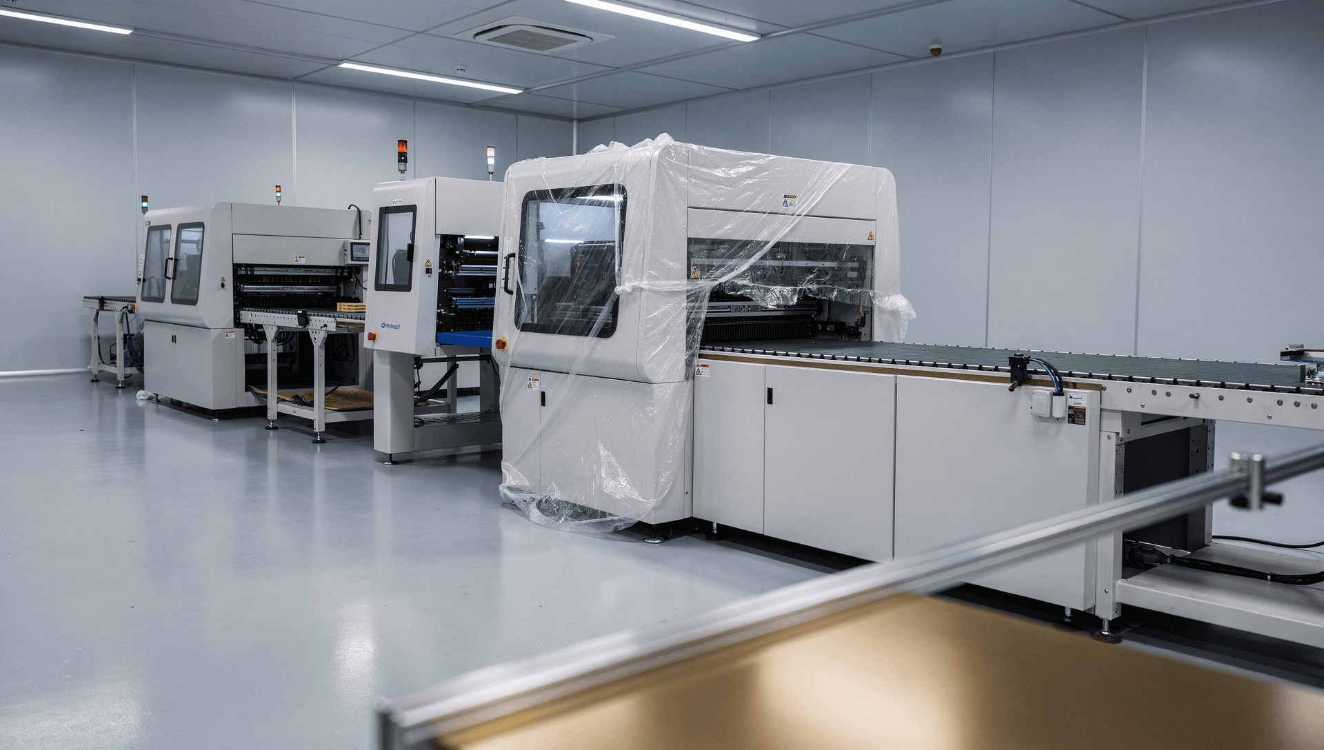 A US electronics surface-mount line being commissioned in a clean facility, a solder-paste printer, pick-and-place machine, and reflow oven part-installed in sequence, cool blue-grey light with a warm brass highlight on a machined rail.